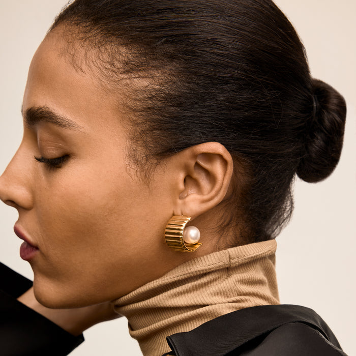 Close-up of a woman wearing gold hoop earrings with a pearl accent. | Lead