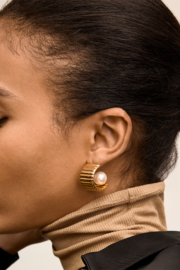 Close-up of a person wearing a gold earring with a pearl accent. | Exclude | Grid