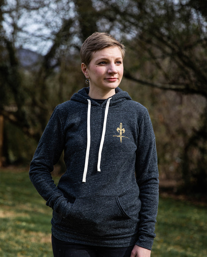 Woman wearing a dark gray hoodie with gold sword and wheat emblem outdoors