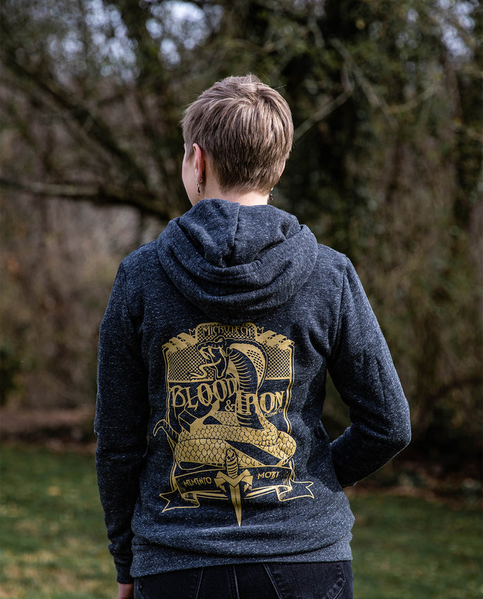 Person outdoors in dark hoodie with gold Blood & Iron cobra and sword graphic on back