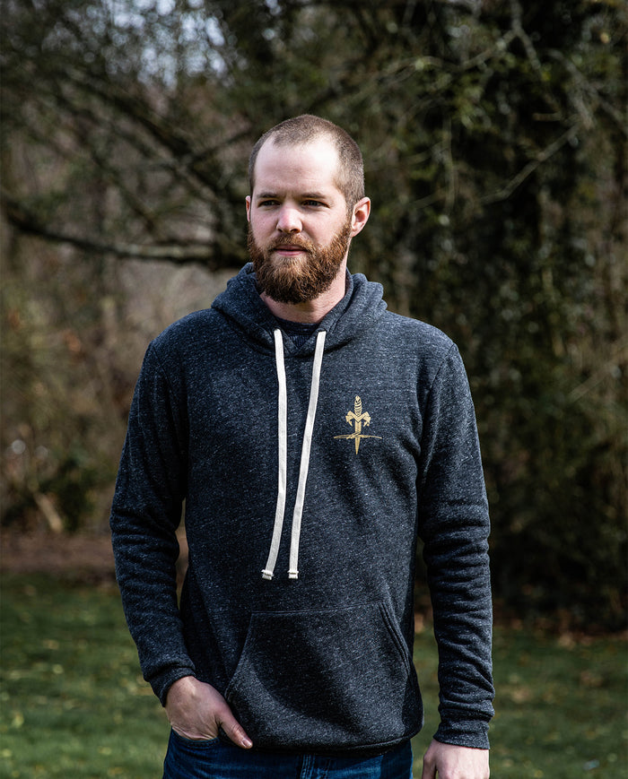 Man wearing dark gray hoodie with gold sword graphic outdoors in a natural setting