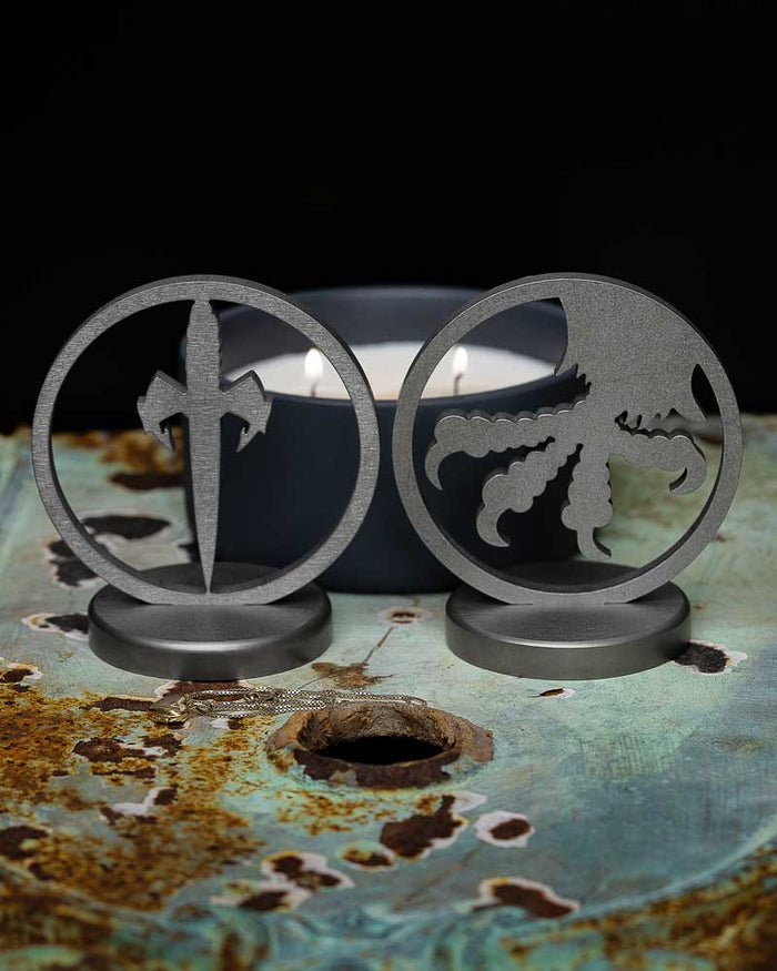 Metal desk stands with sword and octopus cutouts on a rustic table near a lit candle