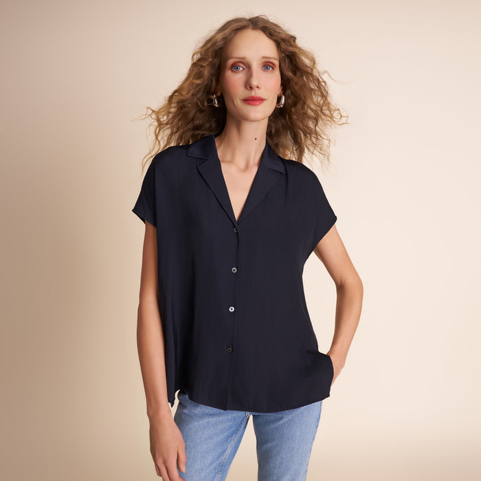 Woman wearing a dark navy short-sleeve blouse with a beige background | Lead