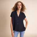 Woman wearing a dark navy short-sleeve blouse with a beige background | Lead