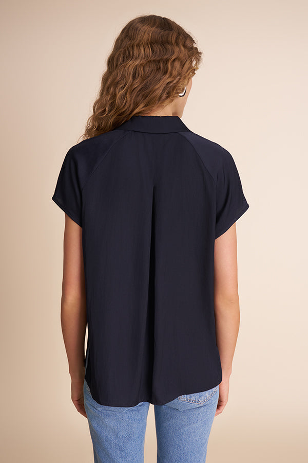 Person wearing a navy blue shirt with short sleeves on a beige background | Grid Hover | Exclude