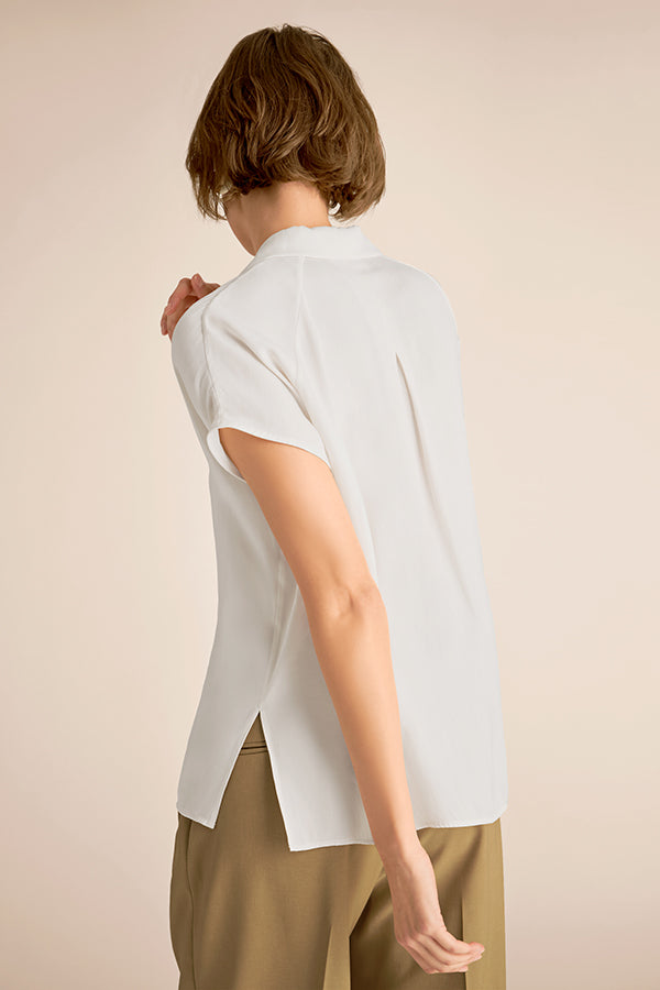 Person wearing a white sleeveless top and beige pants against a beige background | Exclude