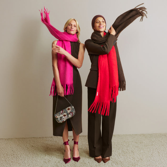 Two women wearing scarves, one pink and one red, against a plain background.
