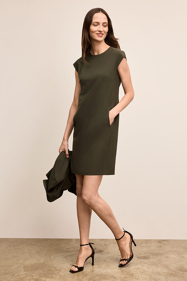 Woman wearing a green dress holding a black jacket against a beige background | Exclude | Grid Hover