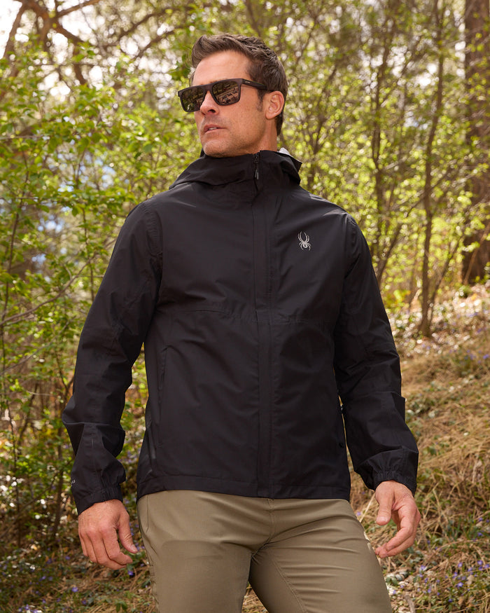 Man wearing a black jacket and sunglasses in a forest setting