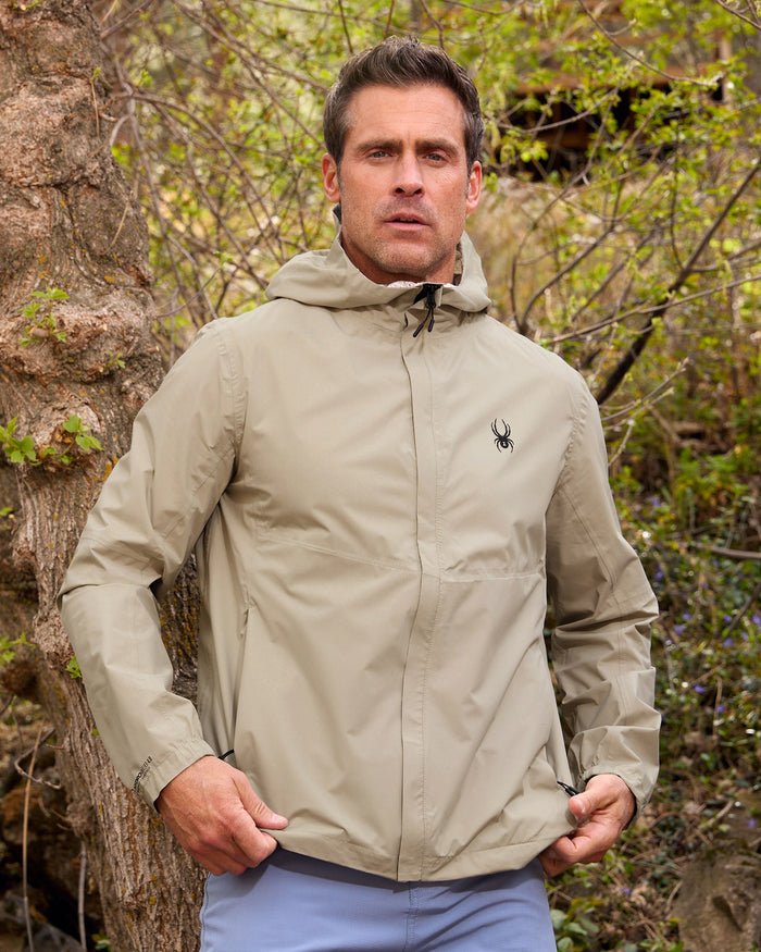 Man wearing a beige jacket with a logo in a forest setting
