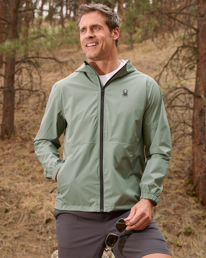 Man wearing a green jacket with a brand logo in a forest setting