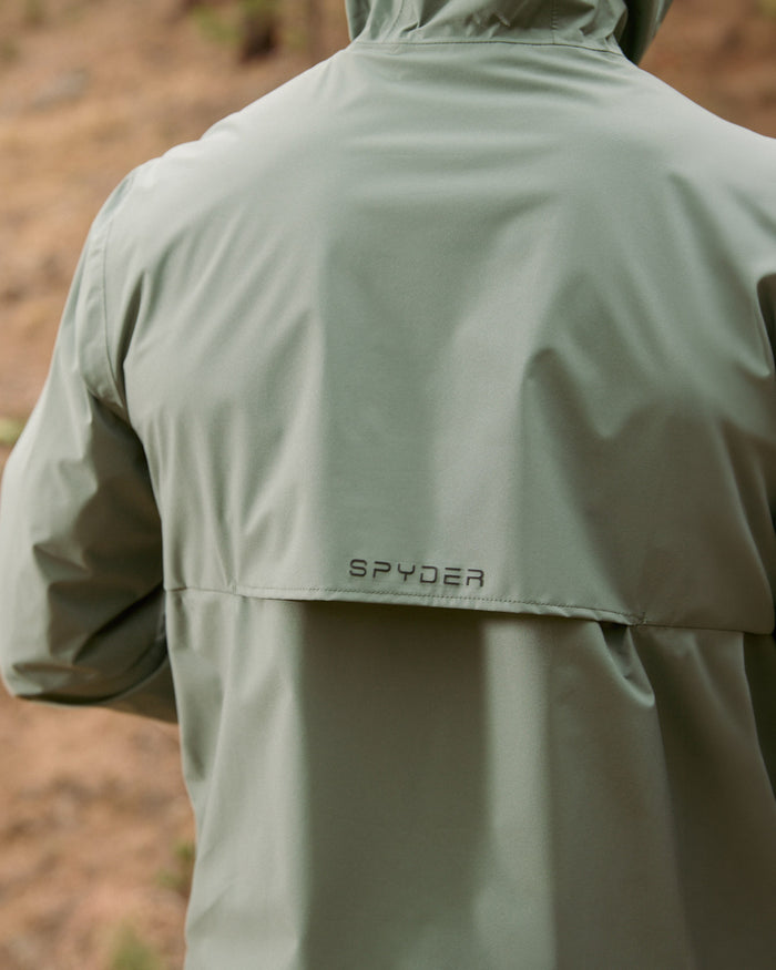 Close-up of a green jacket with 'Spyder' branding on a blurred natural background