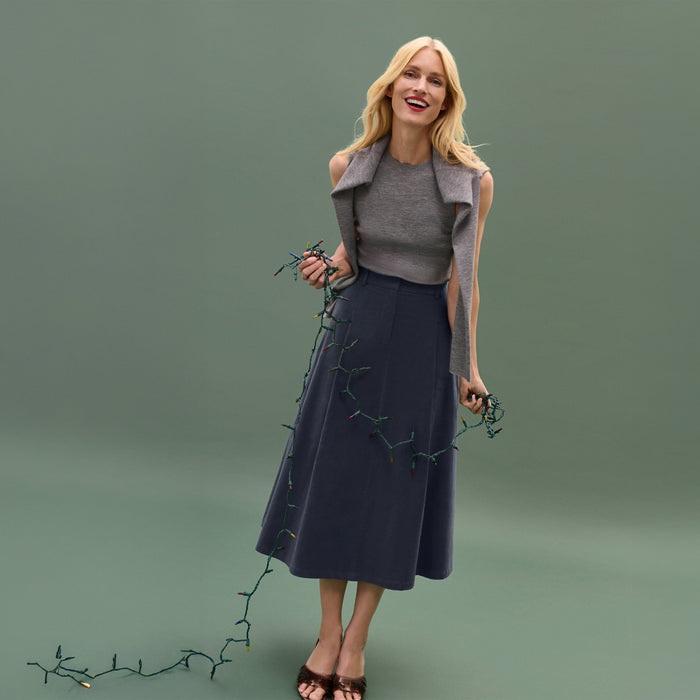 Woman wearing a gray vest and navy skirt holding greenery against a green background