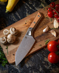 Microtech Culinary Santoku 6" Knife with ember G10 handle, titanium bolsters and stonewashed stainless steel blade on a wooden cutting board surrounded by fresh vegetables and spices. Premium professional kitchen knife for precision chopping and modern cooking.