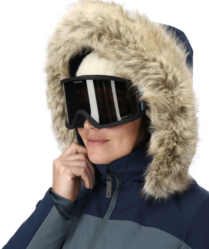 Person wearing a blue winter jacket with a fur-lined hood and black goggles on a white background